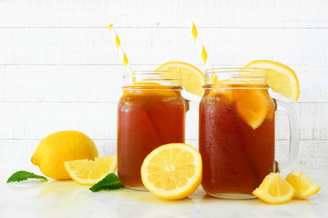 Fototapeta premium Iced tea in mason jar glasses with lemons. Side view on a white wood background.