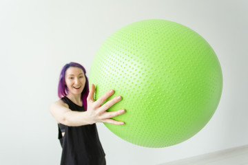 Blurred young positive cheerful girl hipster holding a green fitball in her arms during classes in the gym. Concept of yoga and pilates and fitness.