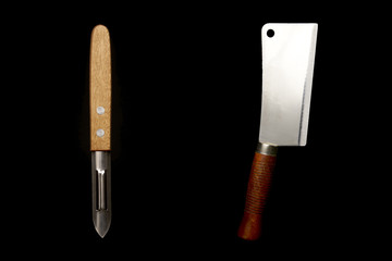 Vegetable peeler versus meat cleaver. Vegan and omnivore battle concept. With copy text space. Isolated on black background. Studio Shot.