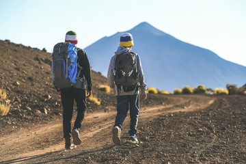 Two young boys walking on a path toward the volcano Teide A couple of tourist child climbing mountain together Italian and Canary island flag on wool caps. Adventure trip togetherness open air concept