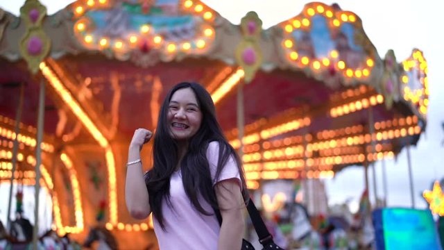 Happy beautiful asian woman at amusement park carnival. Young woman teenager playing carousel travel funfair festival Slow motion.