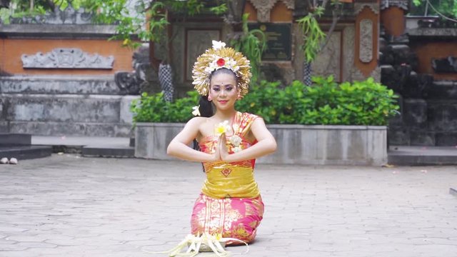 Slow motion of pretty balinese dancer performing while sitting and throwing frangipani flower in the temple