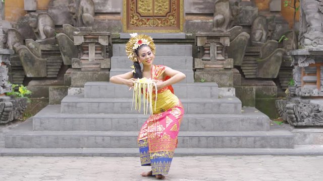 Beautiful balinese dancer posing in the temple while wearing traditional costume and holding frangipani flower. Shot in 4k resolution