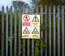 Hazard signs on boundary fence of industrial plant – hidden behind trees - handling dangerous and...