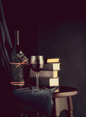 Books, a bottle and a glass with red wine on a black background