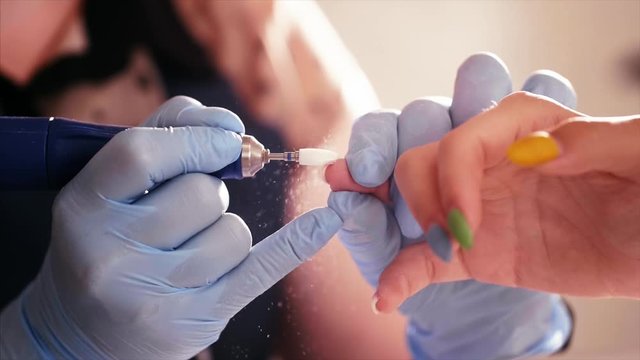 Removal of the shellac with a milling cutter in slow motion, hands in gloves closeup. Master does hardware manicure in the beauty salon.