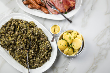 Oldenburger Grünkohl, Kassler Nacken, Kohlwurst und Pinkel auf Platten mit Kartoffeln und Senf auf Marmor Tisch