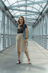 Beautiful stylish woman with backpack, smiling, happy, street style, beige skirt, green t-shirt.