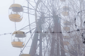 selective focus of ferris wheel attractionron behind barbed wire in fog in winter abandoned...
