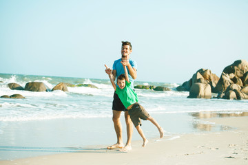 happy family on beach playing, father with son walking sea coast, rocks behind smiling taking vacation