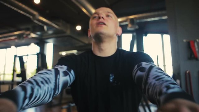 concentrated professional sportsman breathes actively and pulls oar using rowing machine extreme close view