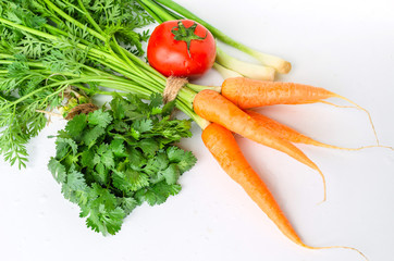 Fresh carrot with green leaves, tomato, onion and parsley on white background.