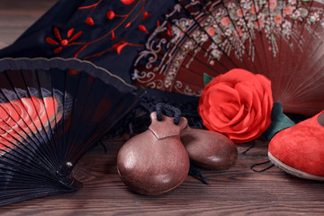 Beautiful and bright accessories for flamenco dance on a wooden background. Castanets, shawl,  fans, shoes  and a flower for the hair.