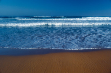 Incoming whitewater waves lapping onto sandy shore