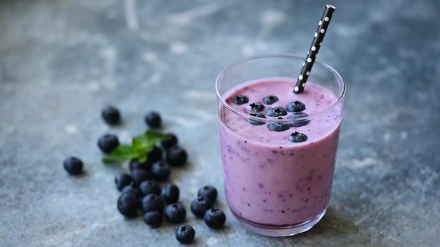 Blueberry smoothie in glass. Girl's hand putting glass of tasty vegan berry smoothie on table