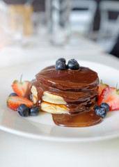 Tasty breakfast. Homemade pancakes with fresh blueberry and melted chocolate on white plate on white background