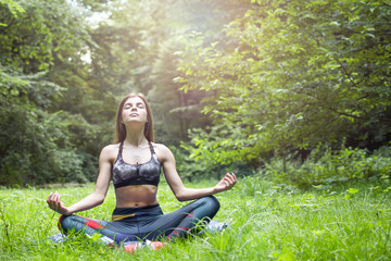 Yoga outdoor. Happy woman doing yoga exercises, meditate in the park. Yoga meditation in nature. Concept of healthy lifestyle and relaxation. Pretty woman practicing yoga on the grass