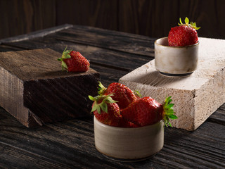 Composition on a wooden, dark background, consisting of fresh strawberries, which lies on the wooden bars of dark and light colors, in small ceramic cups.