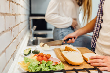 Close up photo of couple in the kitchen making salad, man holding bread.