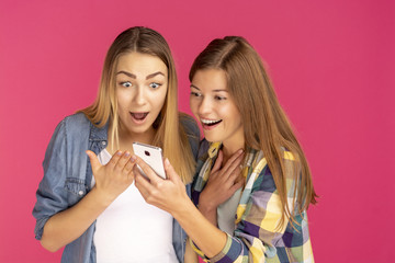 two beautiful girls friends use a smartphone, write sms, pink background