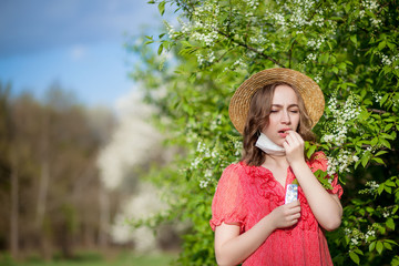 Young girl blowing nose and sneezing in tissue in front of blooming tree. Seasonal allergens affecting people. Beautiful lady has rhinitis.