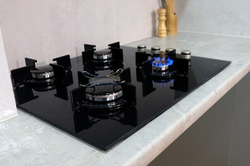 Burning gas on the kitchen gas stove. Black hob from tempered glass on four burners. Flame from a...