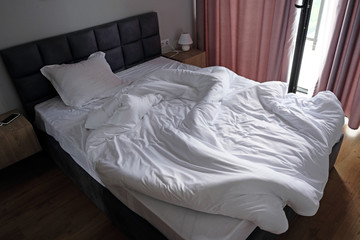 Fototapeta na wymiar Comfortable bed with white linen at home. rumpled bed with white messy pillow decoration in bedroom interior