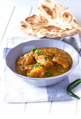 Close up traditional Indian butter chicken curry and lemon served with chapati bread grey bowl whhite wooden background.