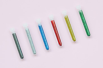 Colorful glitters lies on pastel pink background. Many long bottles with multi-colored bright sparkles for nail polish