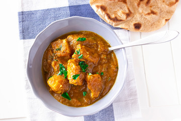 Close up traditional Indian butter chicken curry and lemon served with chapati bread grey bowl whhite wooden background. Top view.