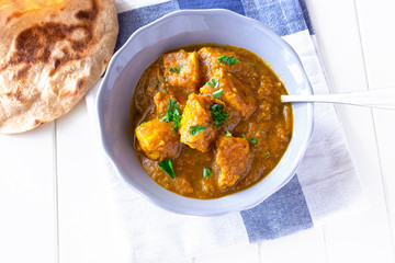Close up traditional Indian butter chicken curry and lemon served with chapati bread grey bowl whhite wooden background. Top view.