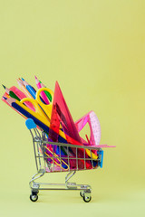 Shopping cart with different stationery on the yellow background