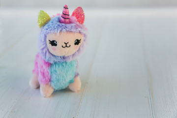 Colored plush llama unicorn on white wooden background
