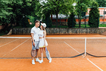 Tennis sport - couple relaxing after playing game of tennis outside in summer. Hugging couple.