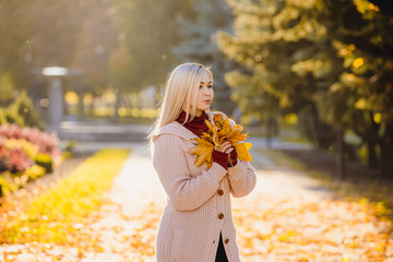 Romantic woman in the fall in the park. Stylish girl holding a golden autumn leaf near the face.
