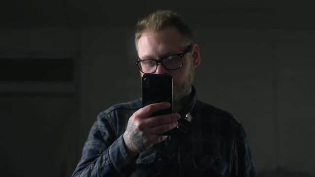 Man in glasses looks carefully to his phone in the dark environment, people with gadgets, surfing the internet, looking through the social networks, chat in the mobila phone, Full HD Prores 422 HQ