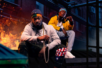 Two black rappers in caps sitting by the fire