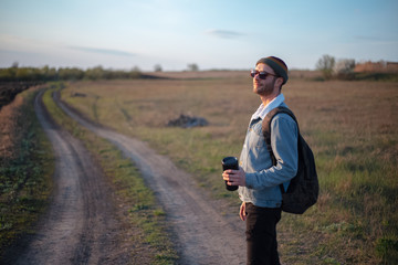 Young man in the green fields with thermo cup with coffee