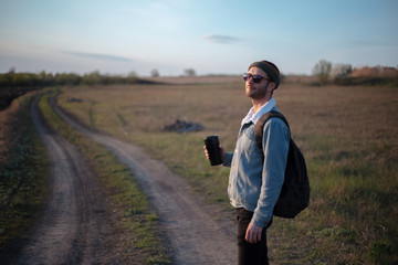 Young man in the green fields with thermo cup with coffee