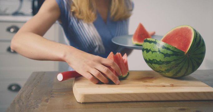 Young woman cutting watermelon and putting pieces on a plate