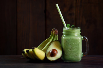 Avocado and banana smoothie in glass jar on wooden background