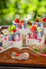 Granola with berries and yoghurt in jar on wooden tray