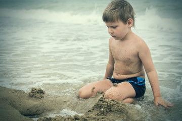 A little boy builds from sand on the seashore, the ocean. Baby is played on the beach.