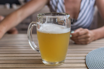 A glass of beer on the table of a summer cafe in front of a woman.