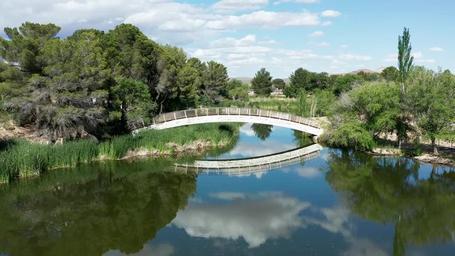 Flying toward picturesque white bridge over reflective lake, sunny day