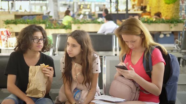 The concept of tourism, recreation and exchange learning. A woman and two teenagers, a boy and a girl, at the airport, a woman using a smartphone