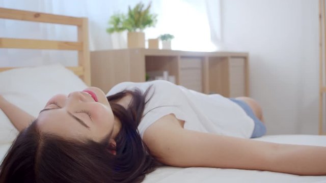 Asian woman smiling funny happy lying on bed in bedroom, Beautiful japanese female using relax time after wake up at home. Lifestyle women using relax time at home concept. Slow motion shot.
