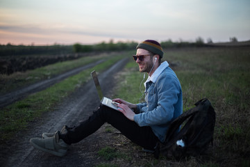 Smiling guy working on laptop with earphones on in the meadowlands 