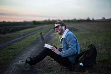 Obraz premium Smiling guy working on laptop with earphones on in the meadowlands 