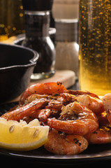 Fried shrimp with lemon on a plate, a glass of beer with bubbles, cast iron frying pan, pepper, salt.